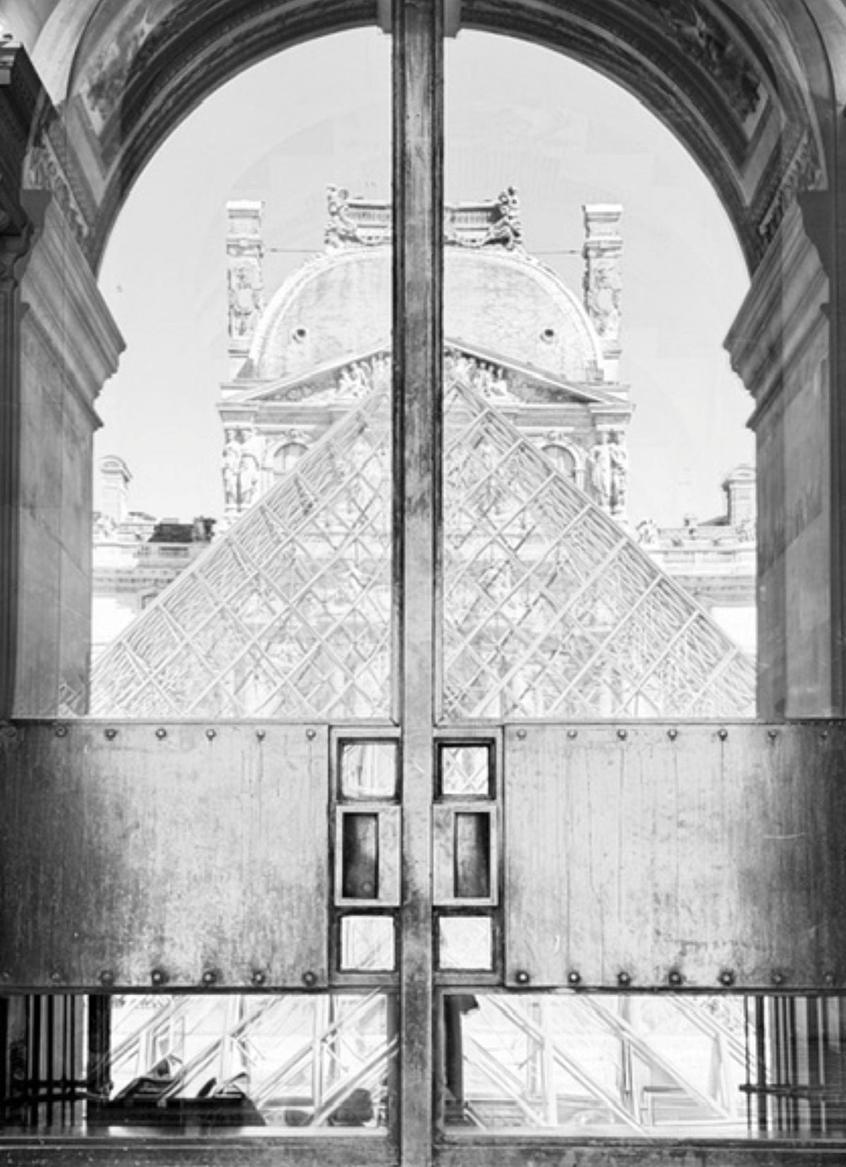 Black and white architectural photograph of the Louvre Pyramid seen through large metal doors framed by a grand arched opening.